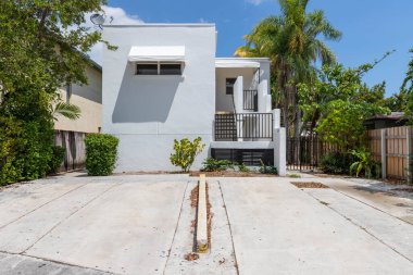 Miami Coral Yolu 'ndaki modern evin önünde garaj yolu, merdivenler, palmiyeler, cyan duvarlar, ahşap çitler, arka planda mavi gökyüzü.