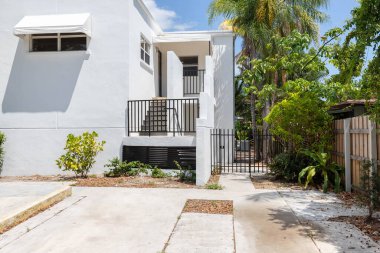 Miami Coral Yolu 'ndaki modern evin önünde garaj yolu, merdivenler, palmiyeler, cyan duvarlar, ahşap çitler, arka planda mavi gökyüzü.
