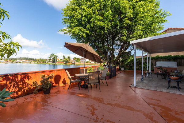 Задний двор оранжевого дома, кафельный пол, растения вокруг, расположенный в Майами в Майами-Даде, Флорида, США, дома в классическом пригороде, голубое небо, наружная мебель, вид на лагуну, деревья.