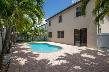 Banliyödeki evin arka bahçesi, taştan detaylar, kırmızı kiremit çatı, Miami-Dade, FL, ABD, yüzme havuzu, taş yataklı çimenler, metal çitler, kısa çimenler ve mavi gökyüzü.