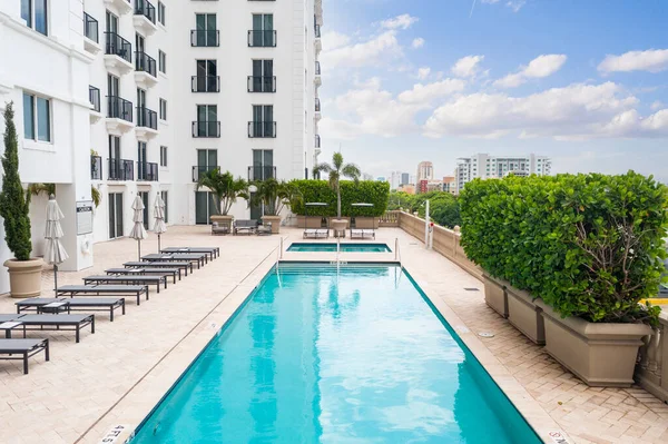 stock image Point of view of the pool, in a hotel with several lounge chairs and umbrellas around, spa, balconies, windows, privet, palms and plants around