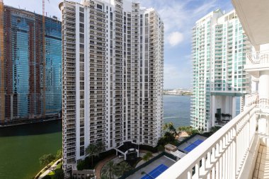 Brickell Key bölgesinin balkon görüntüsü, bir sürü kule ve modern bina, ticari şehir manzarası, deniz ve kanallarla çevrili, yelkenli, rıhtım, köprüler, caddeler, mavi gökyüzü ve turkuaz deniz