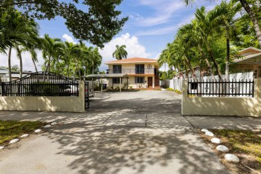 Modern ve klasik evin ön cephesi Coral Gables 'ın banliyöleri, garaj yolu, park yeri, iki katlı bej bina, kiremitli çatı, palmiye ağaçlarıyla çevrili arsa.
