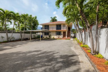 Modern ve klasik evin ön cephesi Coral Gables 'ın banliyöleri, garaj yolu, park yeri, iki katlı bej bina, kiremitli çatı, palmiye ağaçlarıyla çevrili arsa.