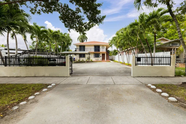 Facade of modern and classic house located in the suburbs of Coral Gables, driveway, parking, two-story beige property, tiled roof, lot surrounded by palm trees