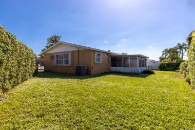 Geleneksel tarz banliyö evi, Miami-dade ilçesinin Westchester mahallesinde, etrafında büyük kısa çim parkı olan terasotta renkli duvarlar, özel çitler, mavi gökyüzü, veranda örtülü