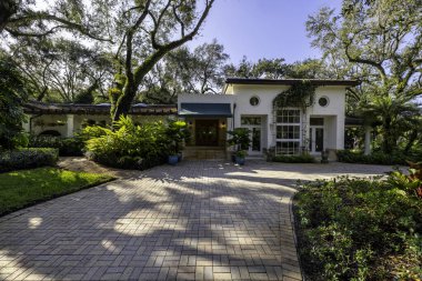 Coral Gables 'daki sömürge konağının ön cephesi, tropikal bitki örtüsü ve çarpıcı bir turkuaz tente ile çevrili, kaldırımlı bir garaj yolu ile bir mimari başyapıttır. Kısa otlar ve mavi gökyüzü bu yeri büyülü kılıyor..