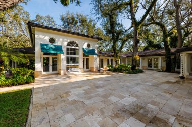 Coral Gables 'daki sömürge konağının ön cephesi, tropikal bitki örtüsü ve çarpıcı bir turkuaz tente ile çevrili, kaldırımlı bir garaj yolu ile bir mimari başyapıttır. Kısa otlar ve mavi gökyüzü bu yeri büyülü kılıyor..