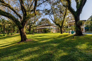 Coral Gables 'daki sömürge konağının ön cephesi, tropikal bitki örtüsü ve çarpıcı bir turkuaz tente ile çevrili, kaldırımlı bir garaj yolu ile bir mimari başyapıttır. Kısa otlar ve mavi gökyüzü bu yeri büyülü kılıyor..
