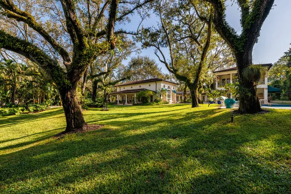 Coral Gables 'daki sömürge konağının ön cephesi, tropikal bitki örtüsü ve çarpıcı bir turkuaz tente ile çevrili, kaldırımlı bir garaj yolu ile bir mimari başyapıttır. Kısa otlar ve mavi gökyüzü bu yeri büyülü kılıyor..