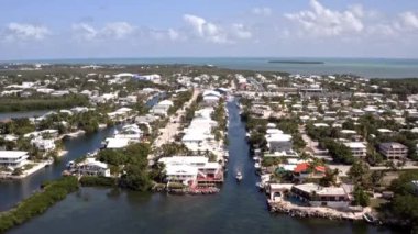 Florida, ABD 'deki hava aracı videosu, ticari alan, lüks evler, binalar ve malikaneler, mavi gökyüzü, okyanus ve tekneleri olan güzel bir sahilde bol miktarda tropikal bitki örtüsü..