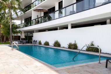 Yüzme havuzlu, ağaçlı, sandalyeli modern bir bina. Mavi gökyüzü, yansıtan havuz ve okyanus, şehir mimarisi ve ABD 'nin Florida kentindeki manzaralı çevre..