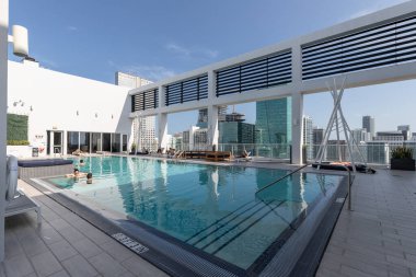 Yüzme havuzlu, ağaçlı, sandalyeli modern bir bina. Mavi gökyüzü, yansıtan havuz ve okyanus, şehir mimarisi ve ABD 'nin Florida kentindeki manzaralı çevre..