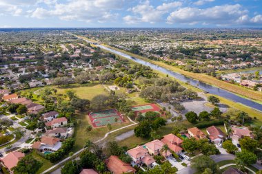 Florida, ABD 'deki hava aracı fotoshoot görüntüleri, ticari alan, lüks evler, binalar ve malikaneler, çevrede bol miktarda tropikal bitki örtüsü, mavi gökyüzü ve botlu su kanalı.