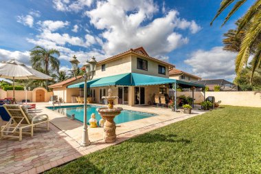 Yüzme havuzlu, ağaçlı, sandalyeli modern bir bina. Mavi gökyüzü, yansıtan havuz ve okyanus, şehir mimarisi ve ABD 'nin Florida kentindeki manzaralı çevre..