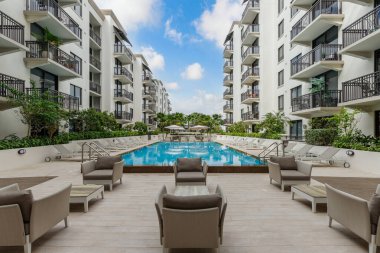 Yüzme havuzlu, ağaçlı, sandalyeli modern bir bina. Mavi gökyüzü, yansıtan havuz ve okyanus, şehir mimarisi ve ABD 'nin Florida kentindeki manzaralı çevre..