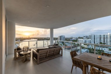 Yüzme havuzlu, ağaçlı, sandalyeli modern bir bina. Mavi gökyüzü, yansıtan havuz ve okyanus, şehir mimarisi ve ABD 'nin Florida kentindeki manzaralı çevre..