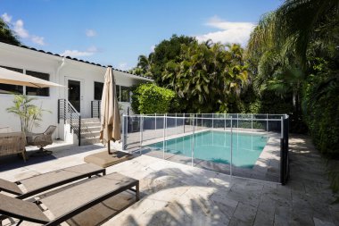 Yüzme havuzlu, ağaçlı, sandalyeli modern bir bina. Mavi gökyüzü, yansıtan havuz ve okyanus, şehir mimarisi ve ABD 'nin Florida kentindeki manzaralı çevre..