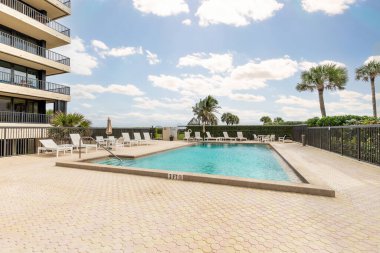 Yüzme havuzlu, ağaçlı, sandalyeli modern bir bina. Mavi gökyüzü, yansıtan havuz ve okyanus, şehir mimarisi ve ABD 'nin Florida kentindeki manzaralı çevre..