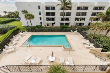 Yüzme havuzlu, ağaçlı, sandalyeli modern bir bina. Mavi gökyüzü, yansıtan havuz ve okyanus, şehir mimarisi ve ABD 'nin Florida kentindeki manzaralı çevre..