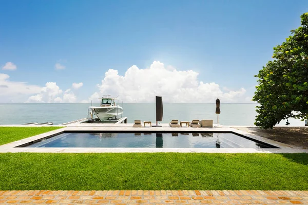 Backyard garden with swimming pool, trees, chairs. Urban landscape with blue sky, reflecting pool and ocean, city architecture, and scenic enviroment in florida, Usa.