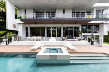 Florida, ABD. Eylül: Yüzme havuzu, yapay çimen, taş zemin, ağaçlar, sandalyeler ve şemsiyesi olan modern bir evin arka bahçesi.