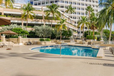 Florida, ABD. Eylül: Yüzme havuzu, yapay çimen, taş zemin, ağaçlar, sandalyeler ve şemsiyesi olan modern bir evin arka bahçesi.