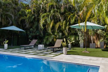 Florida, ABD. Eylül: Yüzme havuzu, yapay çimen, taş zemin, ağaçlar, sandalyeler ve şemsiyesi olan modern bir evin arka bahçesi.