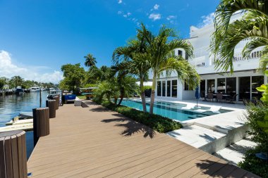 Florida, ABD. Eylül: Yüzme havuzu, yapay çimen, taş zemin, ağaçlar, sandalyeler ve şemsiyesi olan modern bir evin arka bahçesi.