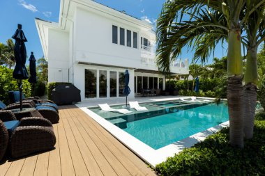 Florida, ABD. Eylül: Yüzme havuzu, yapay çimen, taş zemin, ağaçlar, sandalyeler ve şemsiyesi olan modern bir evin arka bahçesi.