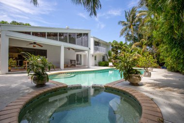 Florida, ABD. Eylül: Yüzme havuzu, yapay çimen, taş zemin, ağaçlar, sandalyeler ve şemsiyesi olan modern bir evin arka bahçesi.