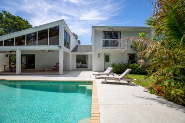 Florida, ABD. Eylül: Yüzme havuzu, yapay çimen, taş zemin, ağaçlar, sandalyeler ve şemsiyesi olan modern bir evin arka bahçesi.