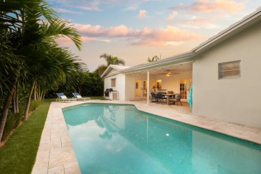 Florida, ABD. Eylül: Yüzme havuzu, yapay çimen, taş zemin, ağaçlar, sandalyeler ve şemsiyesi olan modern bir evin arka bahçesi.