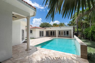 Florida, ABD. Eylül: Yüzme havuzu, yapay çimen, taş zemin, ağaçlar, sandalyeler ve şemsiyesi olan modern bir evin arka bahçesi.
