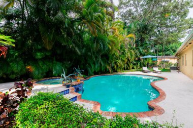 Florida, ABD. Eylül: Yüzme havuzu, yapay çimen, taş zemin, ağaçlar, sandalyeler ve şemsiyeli modern bir evin arka bahçesi.