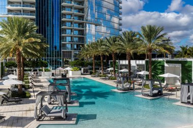 Florida, ABD. Eylül: Yüzme havuzu, yapay çimen, taş zemin, ağaçlar, sandalyeler ve şemsiyeli modern bir evin arka bahçesi.