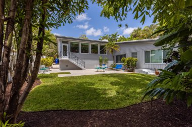 Florida, ABD. Ocak: Yüzme havuzu, yapay çimenler, taş patika, ağaçlar, sandalyeler ve şemsiyesi olan modern bir evin arka bahçesi.