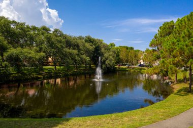 Yeşillik ve parkta bir çeşme ile çevrili güzel bir gölet manzarası.