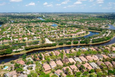 Florida, ABD 'deki hava aracı fotoshoot görüntüleri, ticari alan, lüks evler, binalar ve malikaneler, çevrede bol miktarda tropikal bitki örtüsü, mavi gökyüzü ve botlu su kanalı.