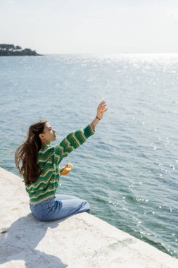 Türkiye 'de iskelede otururken elinde ekmek tutan genç bir kadının yan görüntüsü 