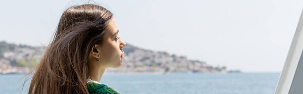 Side view of young brunette woman looking at blurred sea and Princess islands in Turkey, banner 