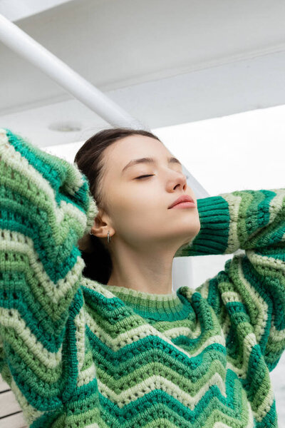 Young woman in knitted sweater touching hair on yacht at daytime 