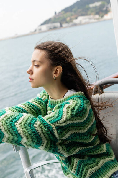 Side view of young woman in knitted sweater traveling on yacht in Turkey 