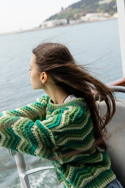 Side view of young brunette woman in knitted sweater looking at sea during cruise on yacht in Turkey 