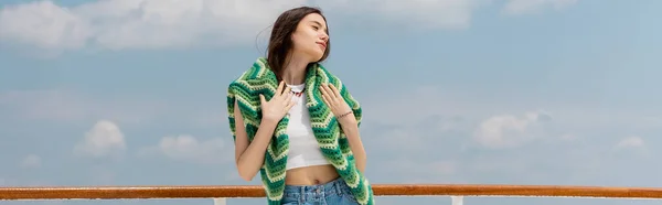 stock image Pretty young woman touching knitted sweater with sky at background, banner 