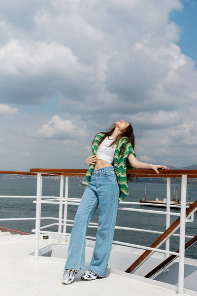 Young woman in sweater and jeans standing near railing of yacht in Turkey 