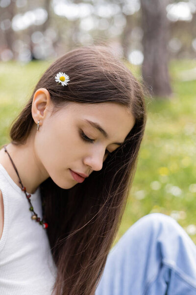 Brunette woman with daisy in hair spending time in park 