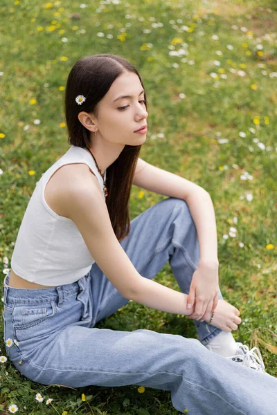 一位头发长满鲜花的年轻女子坐在公园的草坪上 — 图库照片
