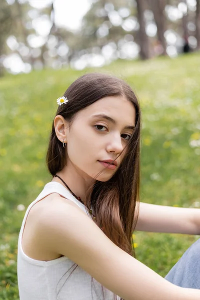 stock image Portrait of brunette woman in top with daisy in hair looking at camera in park 