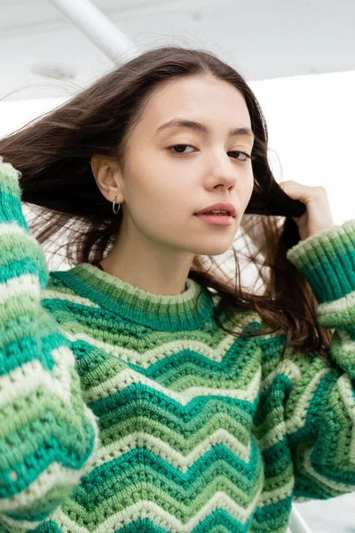 Portrait of young woman in sweater touching hair and looking at camera during trip on yacht — Stock Photo